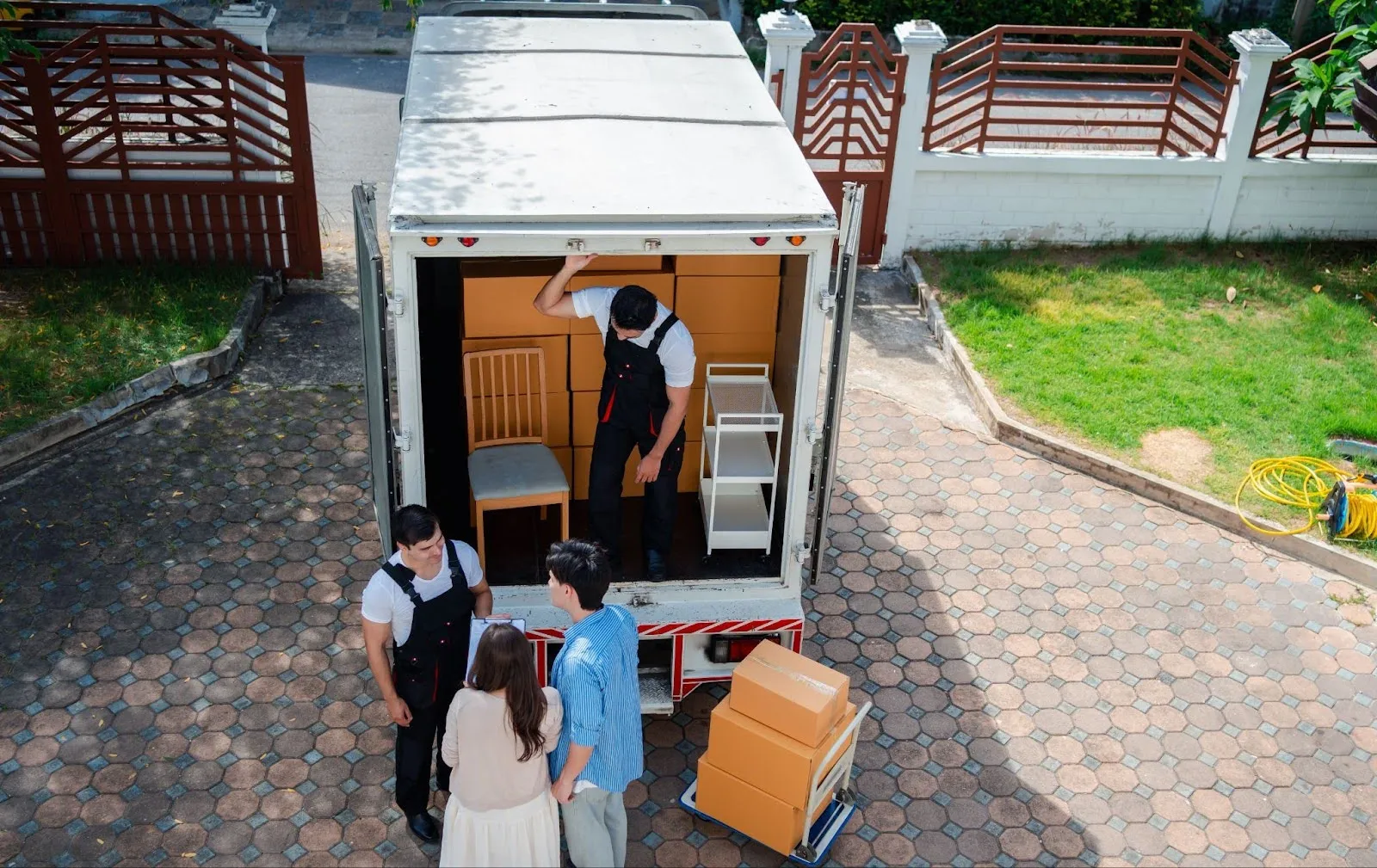 Aerial shot of two movers along with young homeowners standing outside of a moving truck